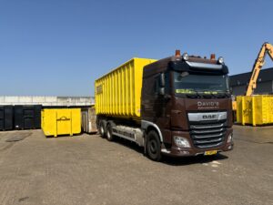 Vrachtwagen met gele container voor het ophalen van schroot